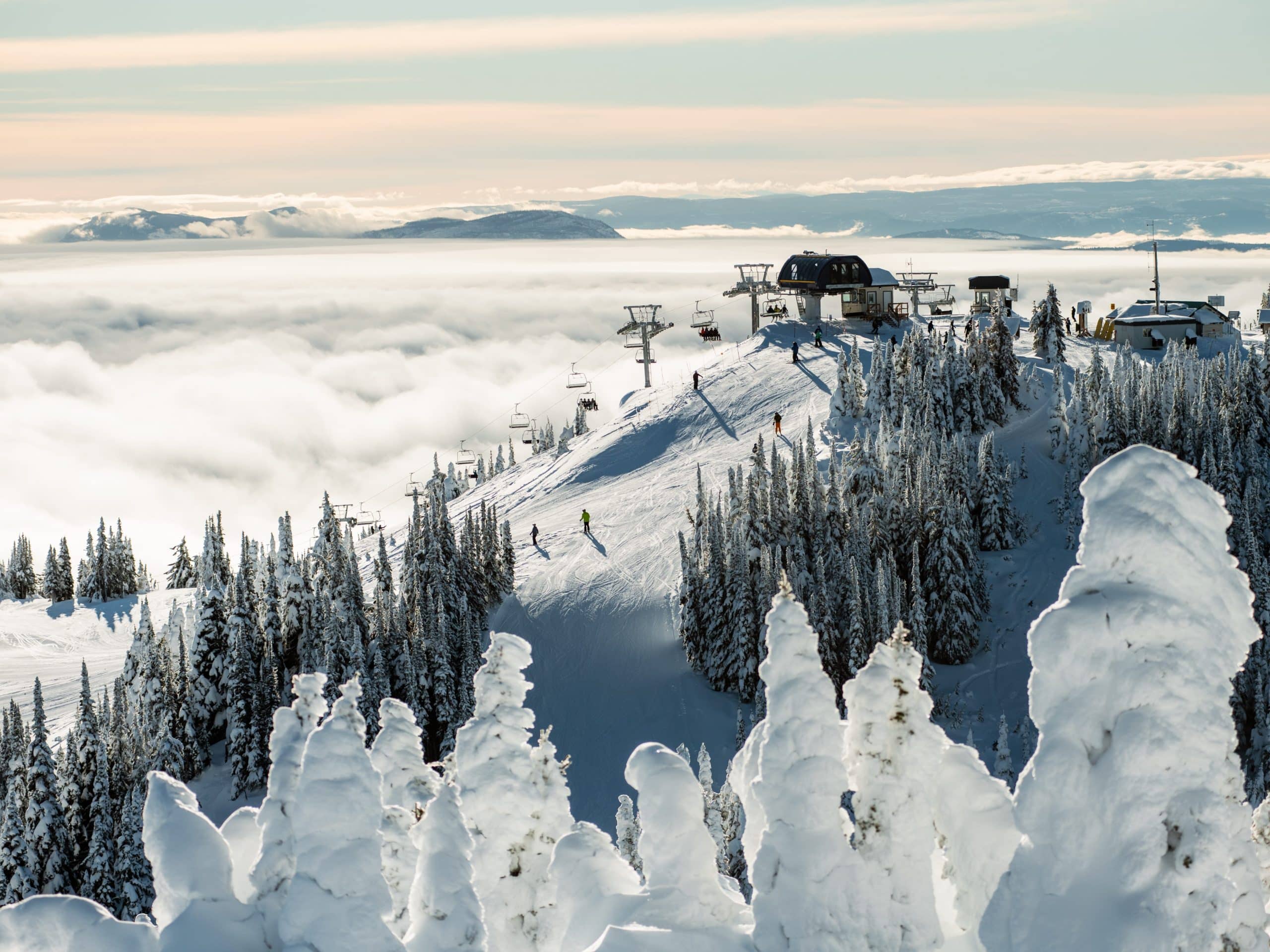 Thick fog rolling in below the crest of a snowy mountain as a chairlift operates.