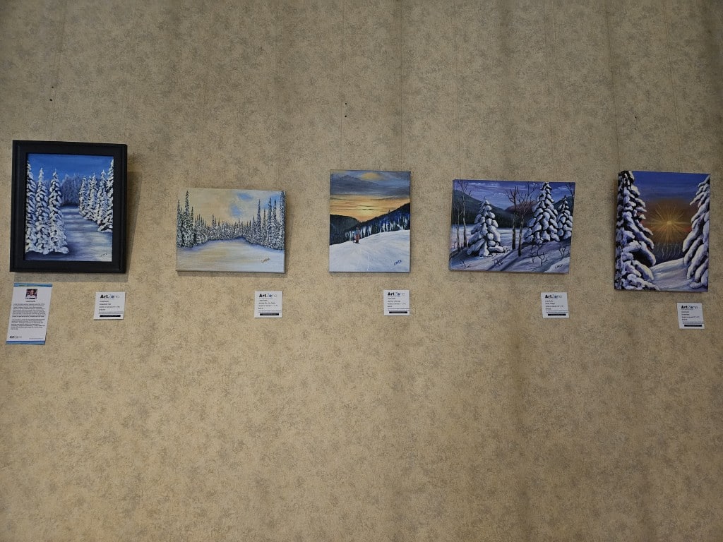 Paintings of winter landscapes displayed in a row on a textured wall.