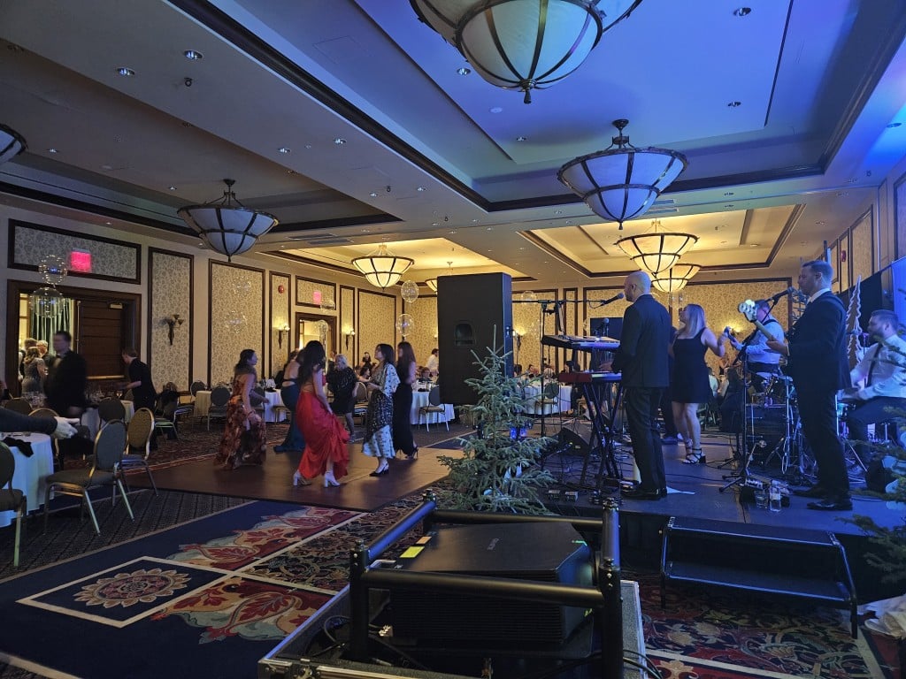 In a darkened ballroom, a band plays and dressed up people dance.
