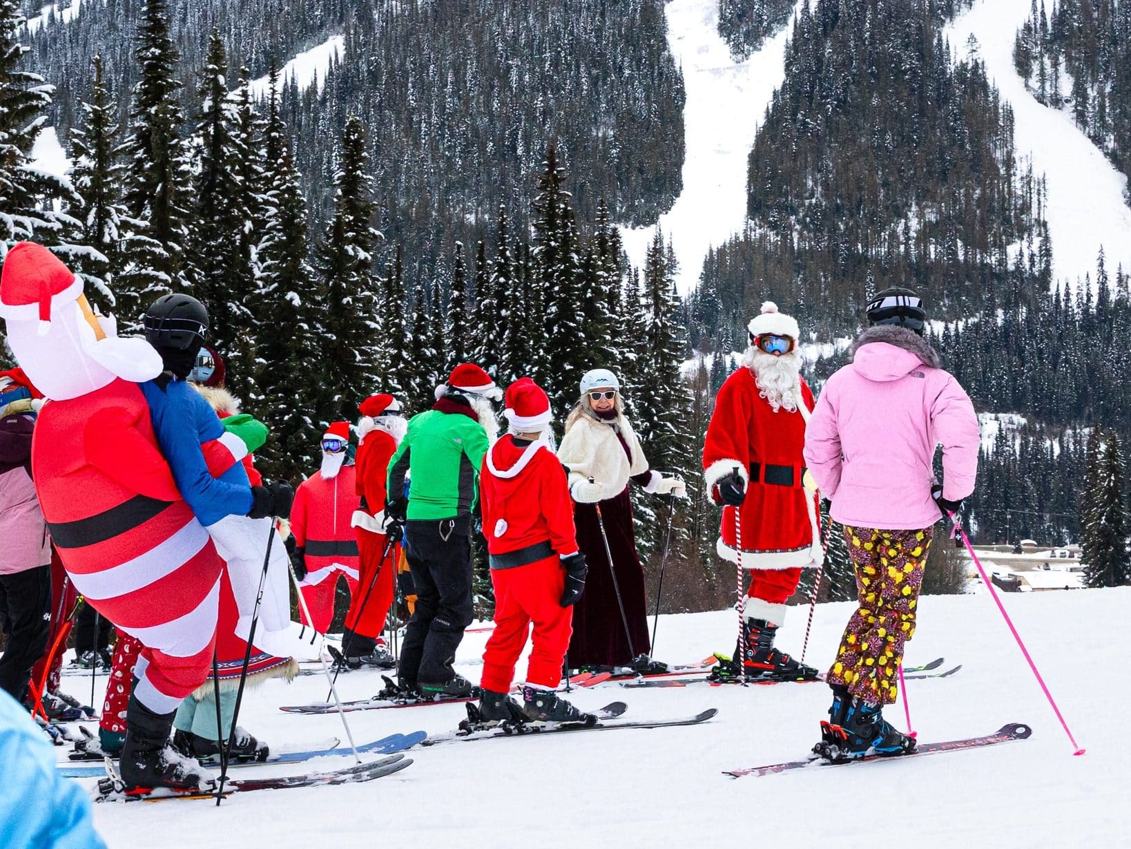 a large group of skiers dressed as Santa stop at the top of a slope.