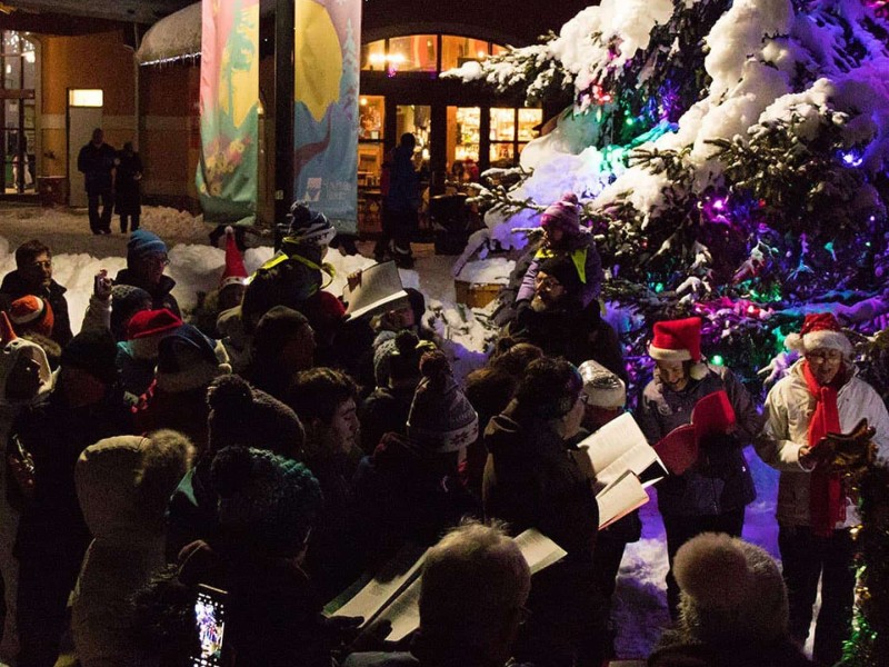 Christmas carolers gather around a lit up tree in Sun Peaks village.