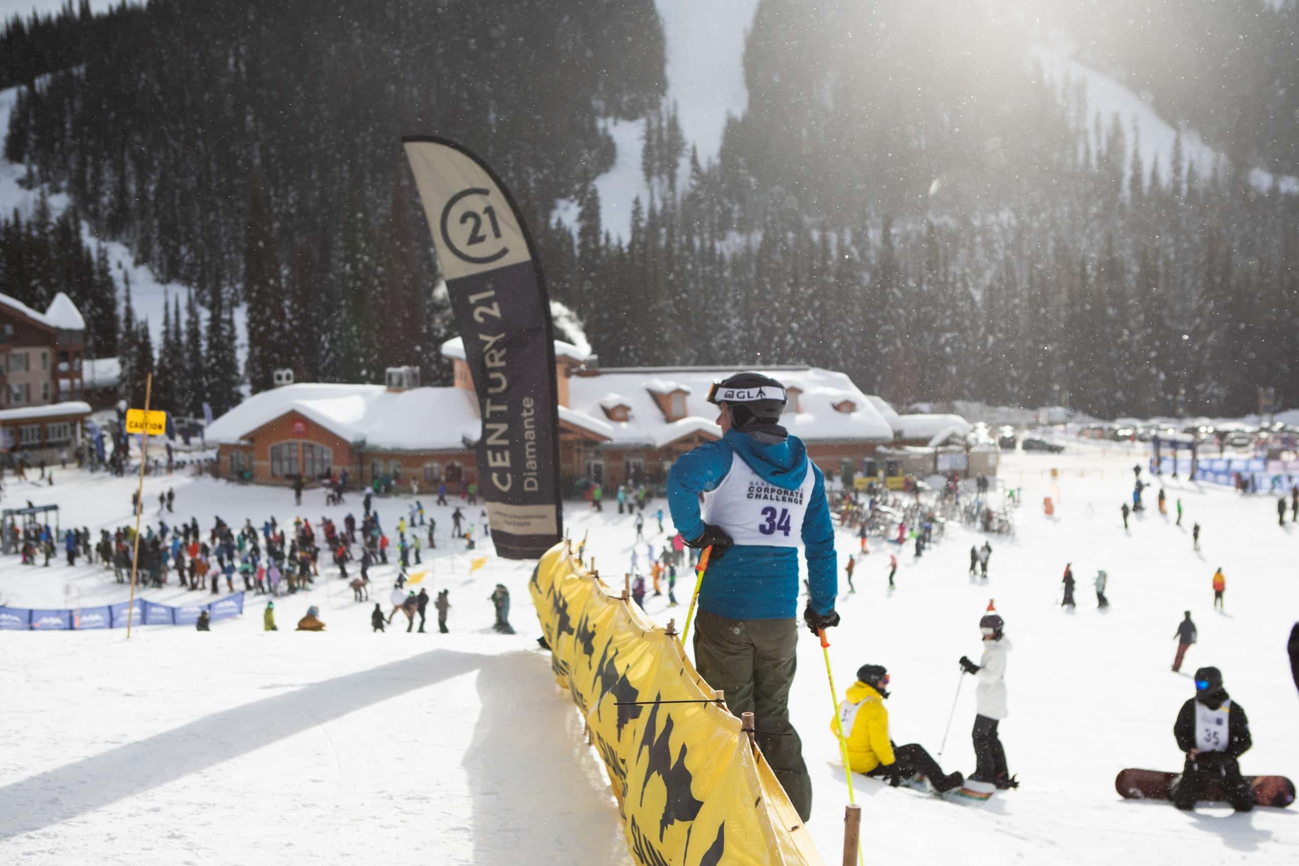 Overlooking a crowd at the village base, the shot focuses on a ski racer by a gate and sign.