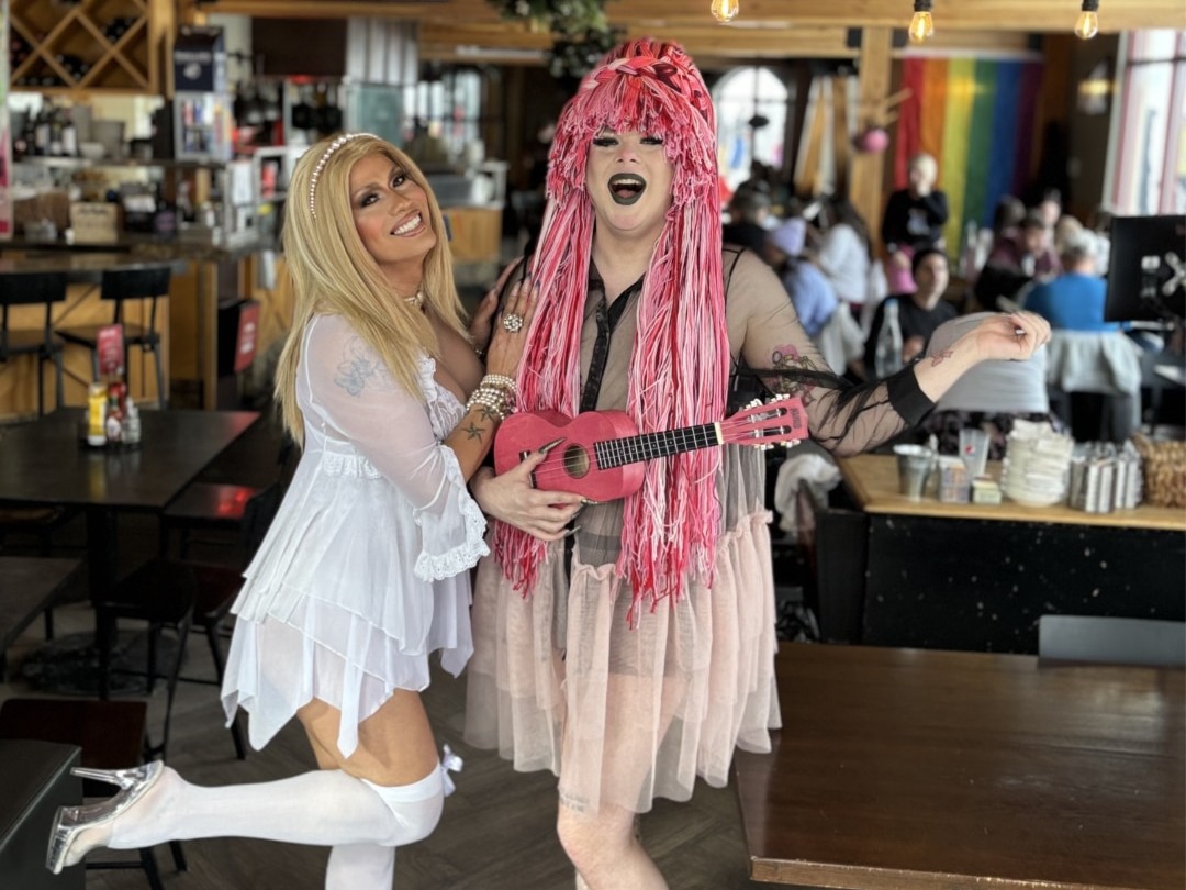 Drag brunch highlights two performers in the front of the frame, with bright pink and white outfits.